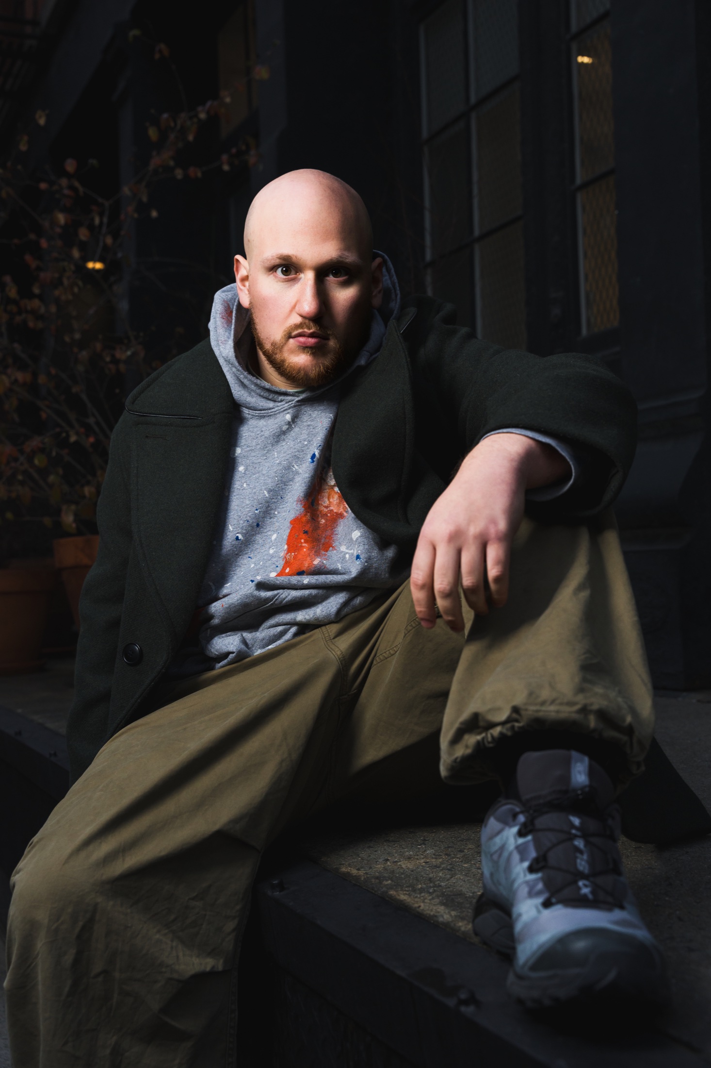 JAKE BACK seated in a dark coat and paint-marked hoodie